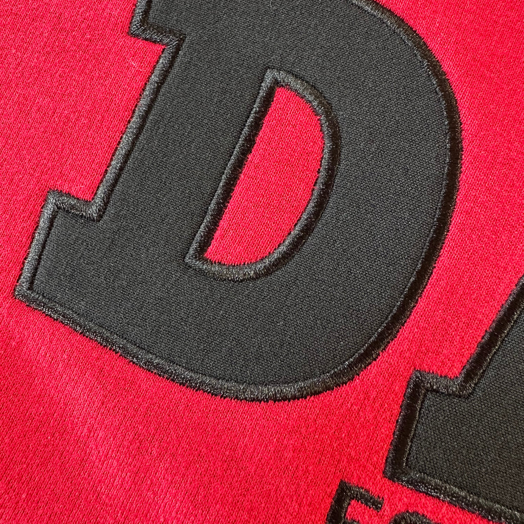Black applique embroidered letter 'D' on red fabric