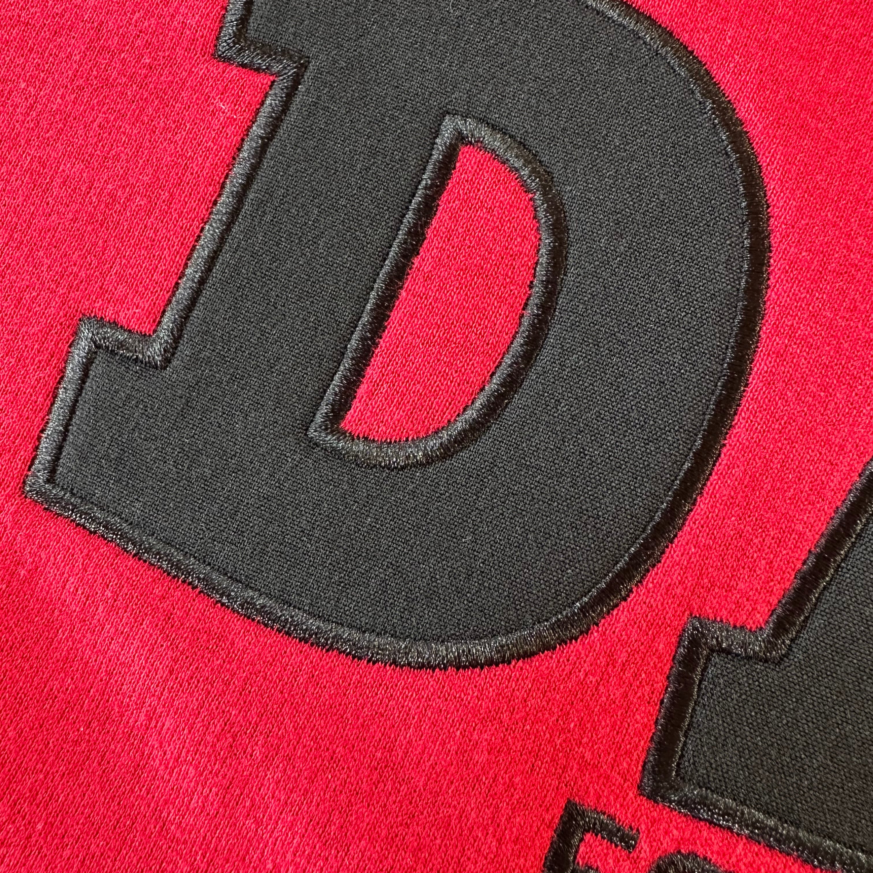 Black applique embroidered letter 'D' on red fabric