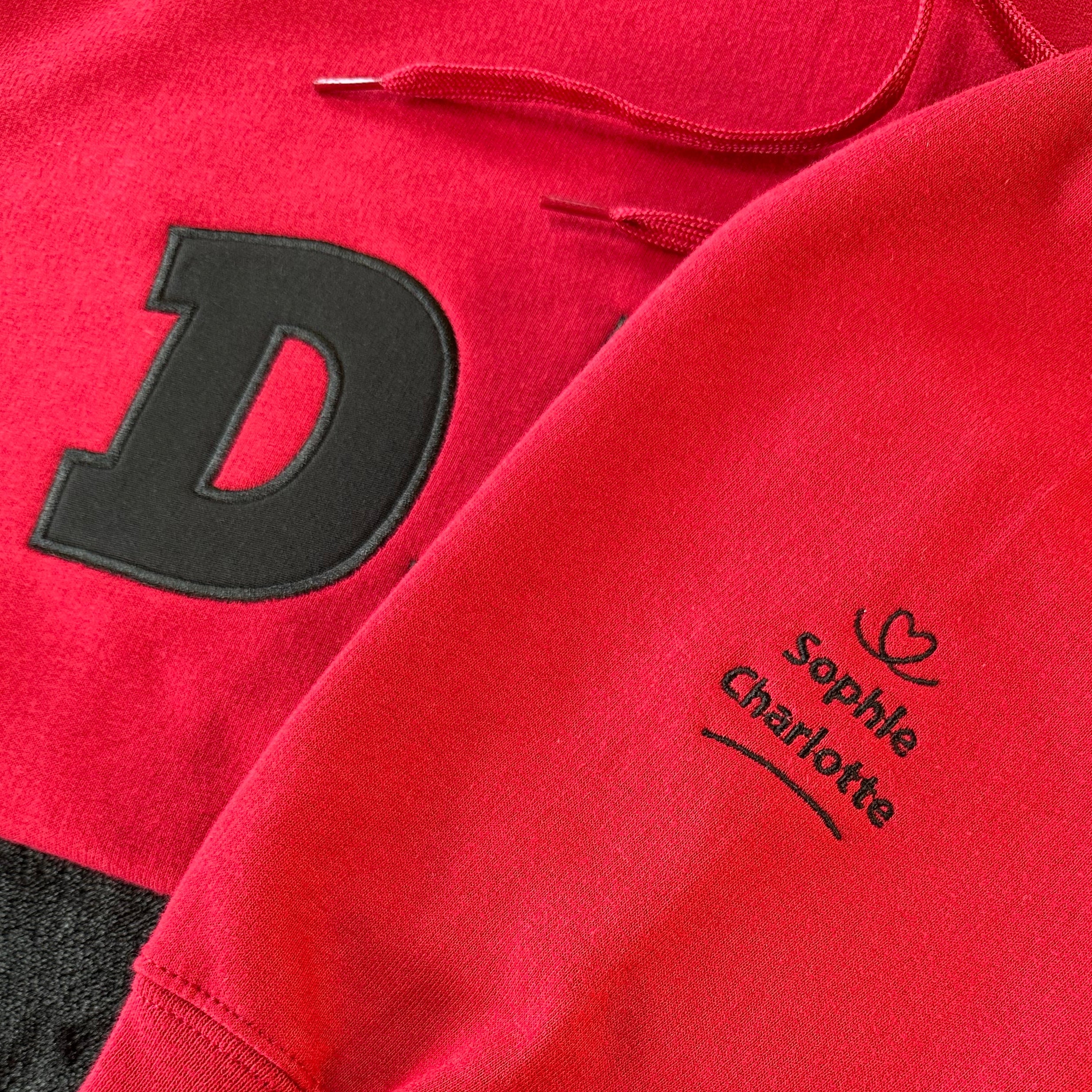 Red hoodie with black letter 'D' and names on a sleeve